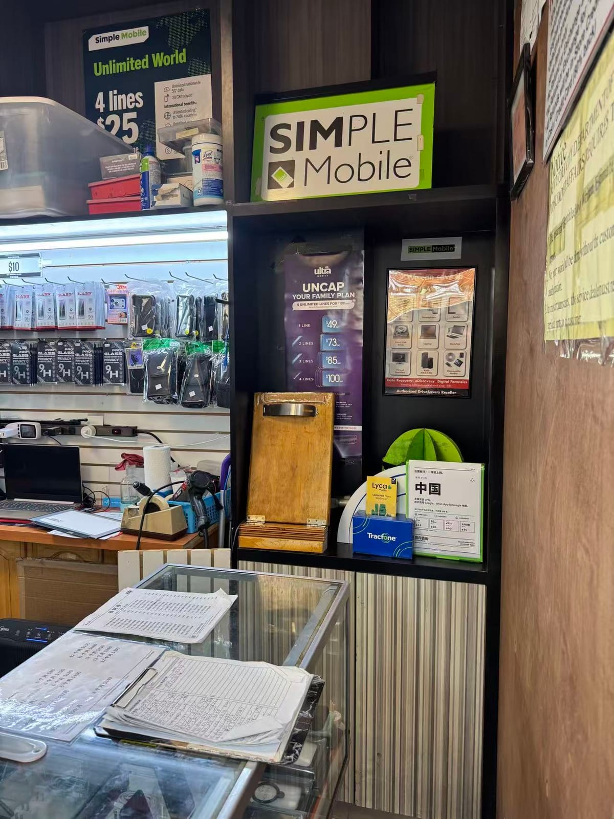 電信展示區:Simple Mobile 與 Ultra Mobile 方案海報,旁邊是手機殼和鋼化膜掛牆,架上放著中國 eSIM 說明卡